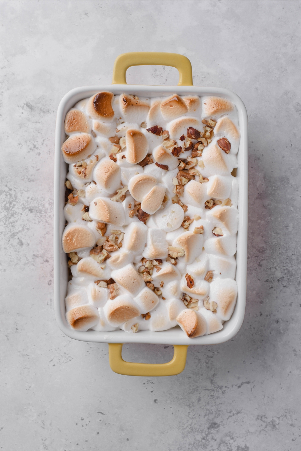 A white and yellow baking dish filled with sweet potato casserole topped with toasted marshmallows and chopped pecans.