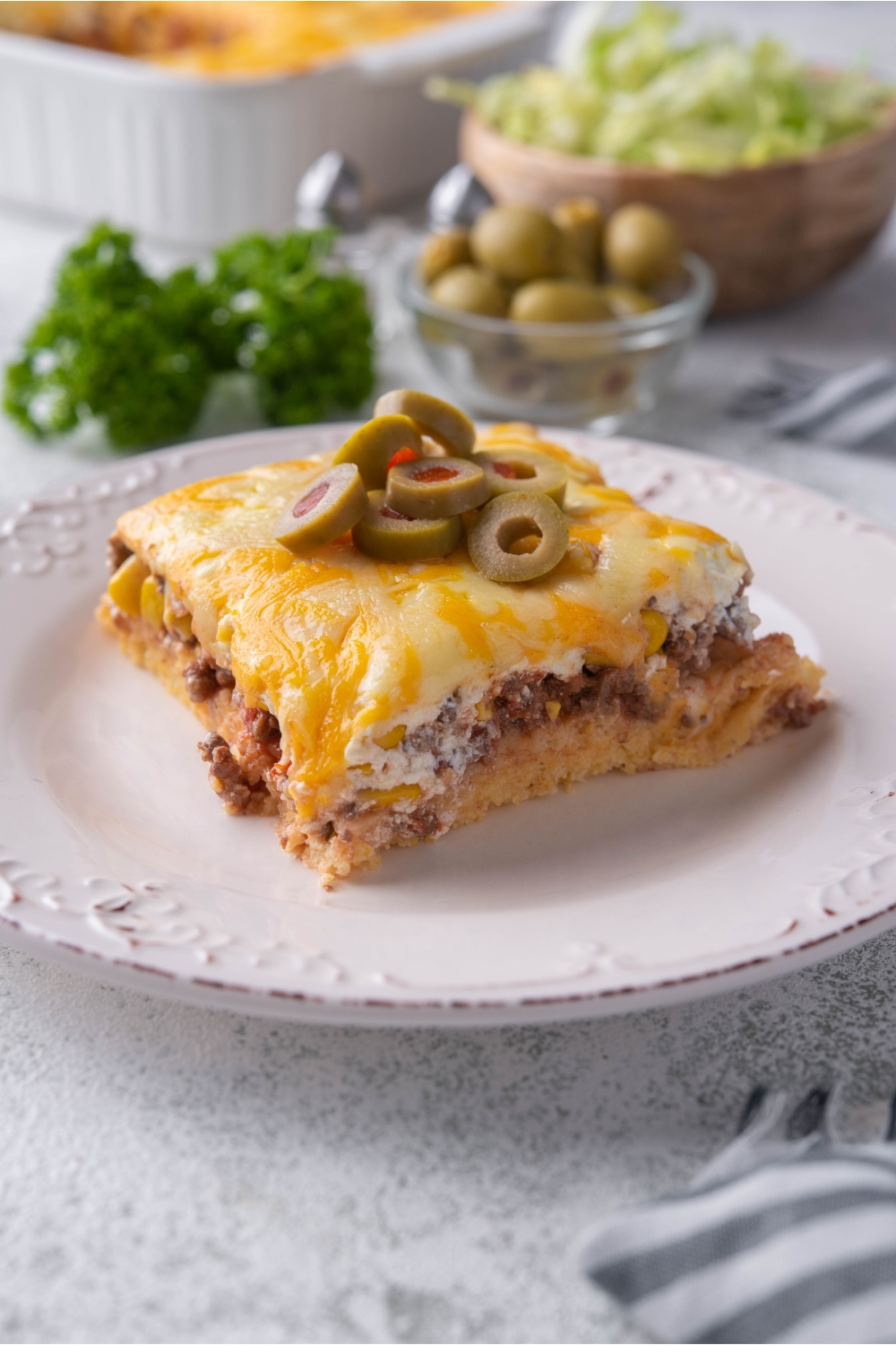 A serving of cornbread taco casserole on a white plate with a garnish if sliced green olives.