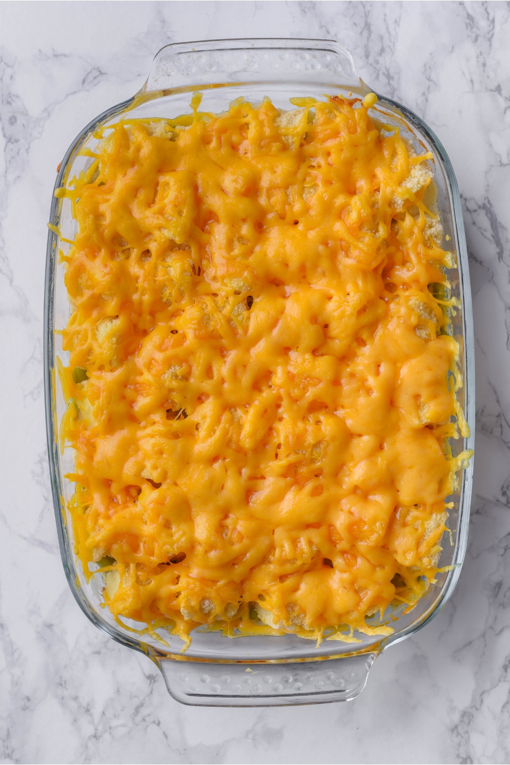 A clear baking dish with freshly baked tater tot and green bean casserole that's covered in shredded cheese.