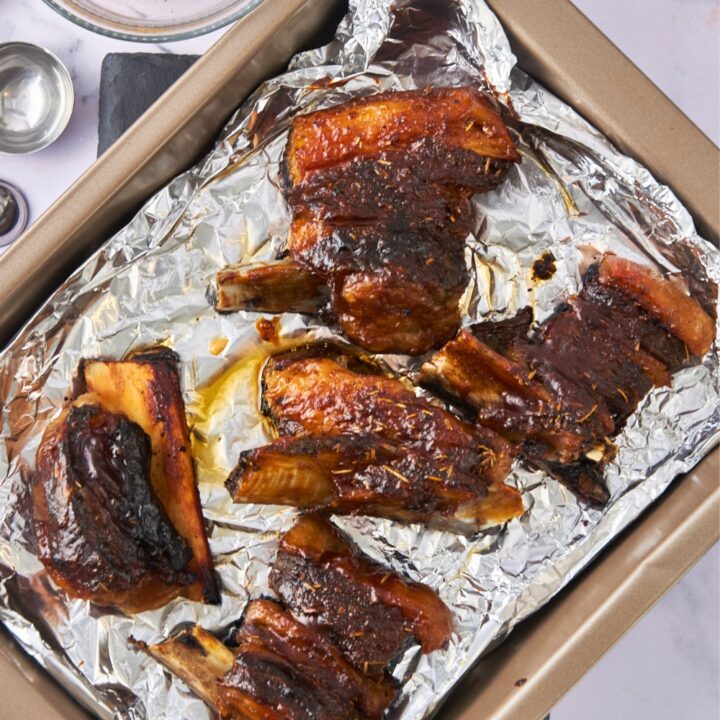 A bunch of beef back ribs on aluminum foil on a baking sheet.