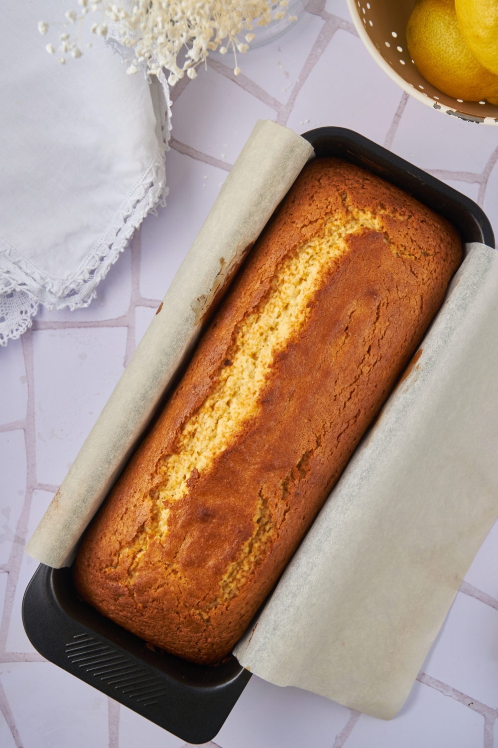 A baked lemon loaf in a loaf pan lined with parchment paper.