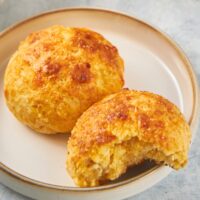 Two cheddar bay biscuits on a plate. The front biscuit has a bite out of it.