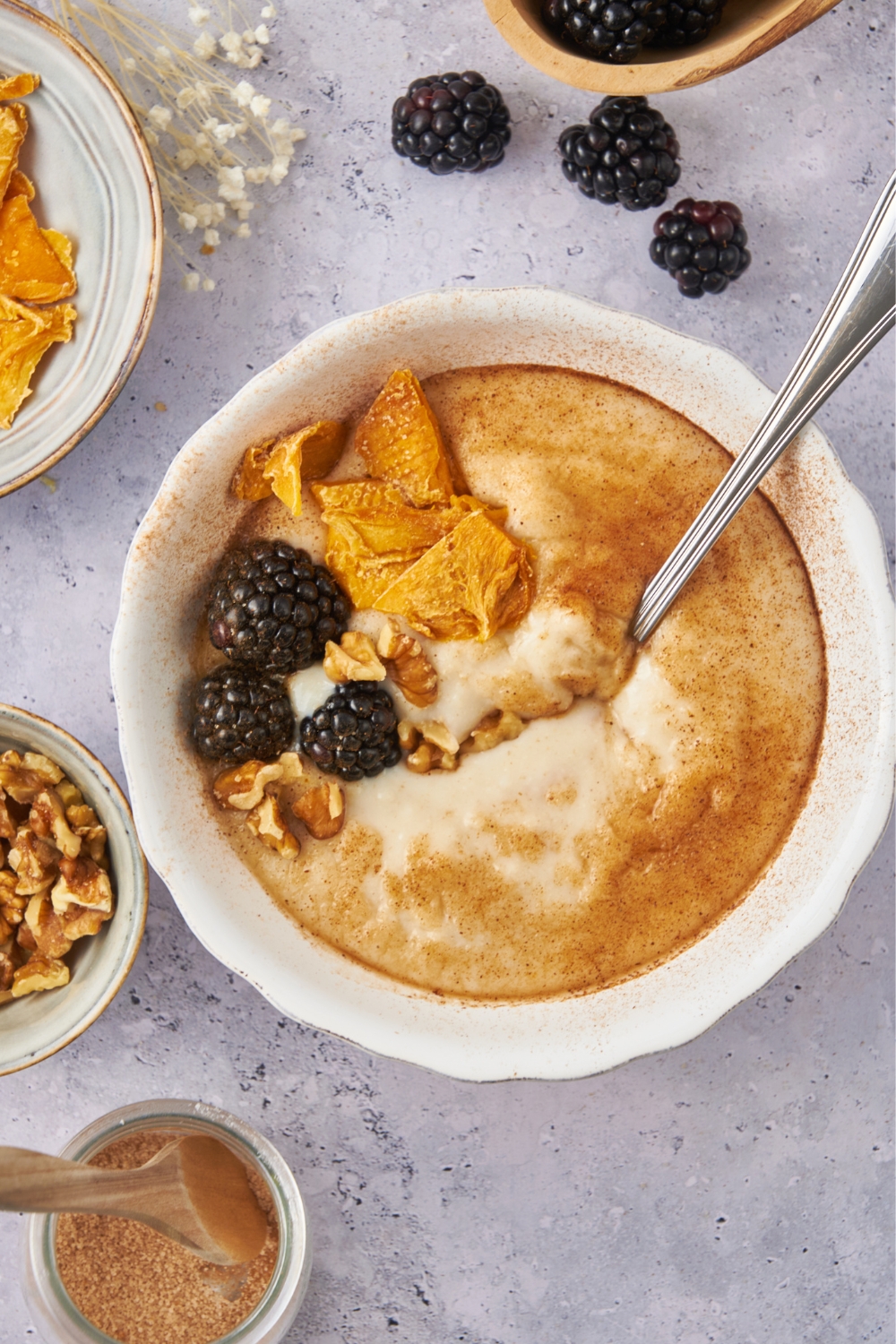 A bowl with cream of wheat topped with cinnamon, berries, dried mango, and walnuts. A spoon is in the bowl.