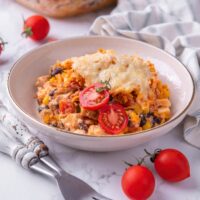 Melted cheese on top of a dorito chicken casserole in a white bowl.