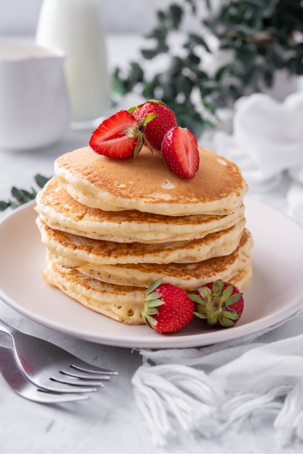 A stack of pancakes on a plate with sliced strawberries.