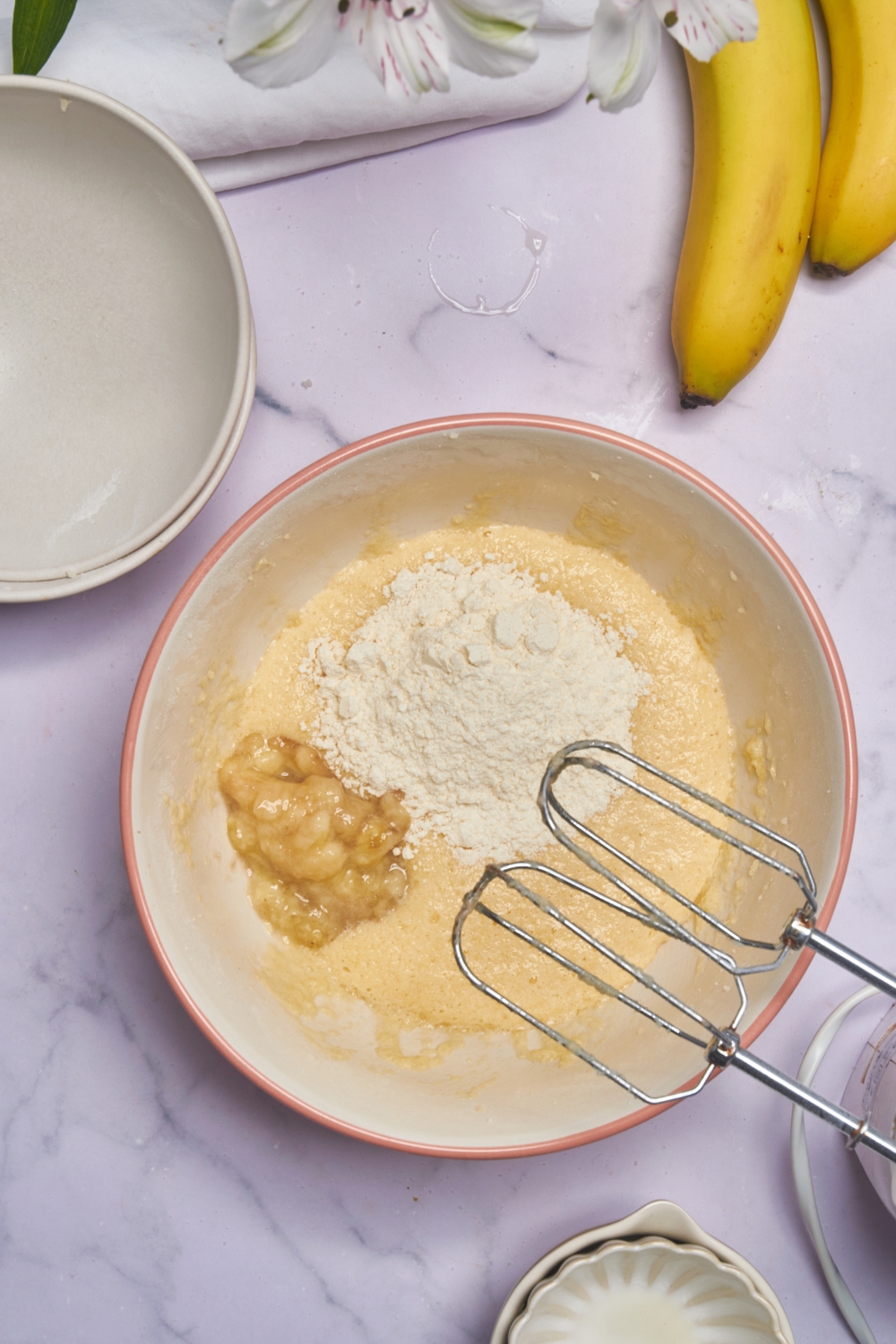 A mixing bowl with flour and mashed banana being added to the wet ingredients.