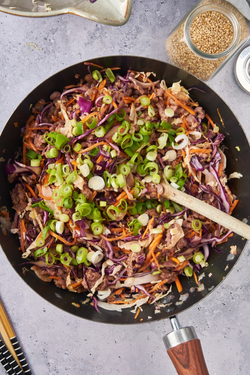 A skillet with the cooked coleslaw topped with green onions.
