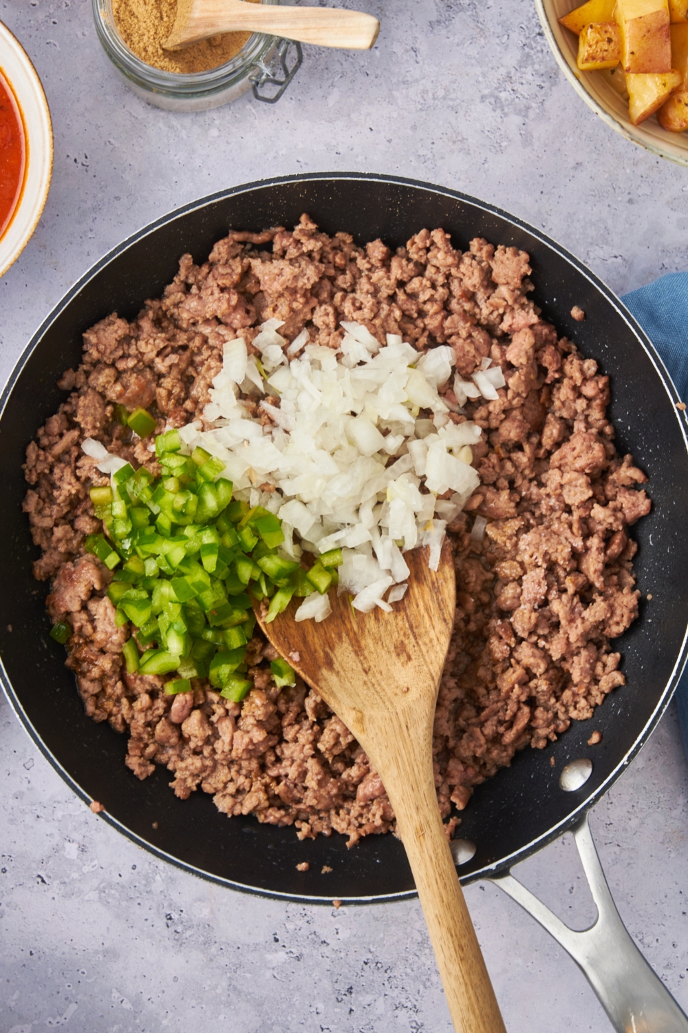 A large skillet with cooked ground beef, onions and pepper have been added.
