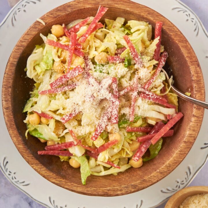 Salami, parmesan cheese, garbanzo beans, and shredded lettuce in a wooden salad bowl on a white plate.