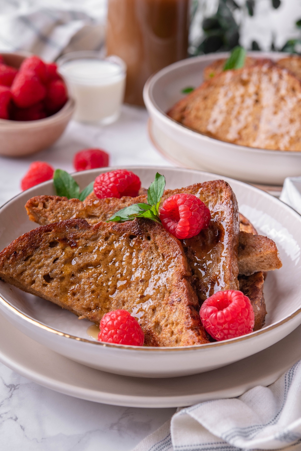 A shallow serving bowl with homemade french toast drizzled with syrup and topped with raspberries.