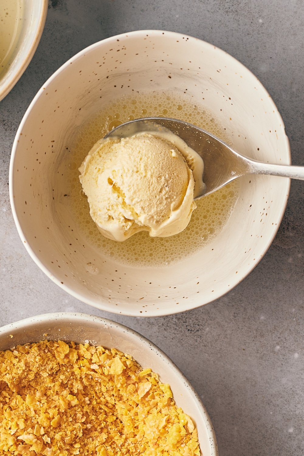 A mixing bowl with beaten egg whites, a spoon is holding hey scoop vanilla ice cream.