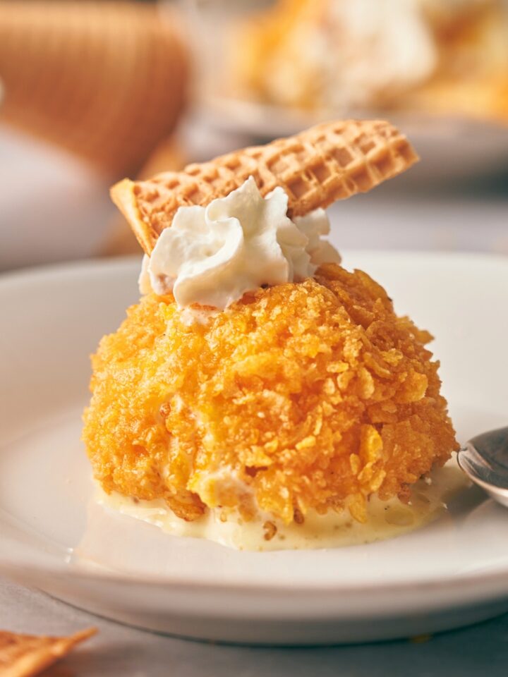A fried ice cream ball with whipped cream and a waffle cone on top.