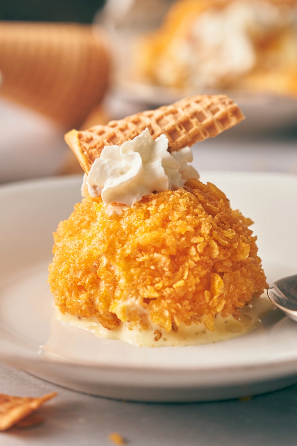 A fried ice cream ball with whipped cream and a waffle cone on top.