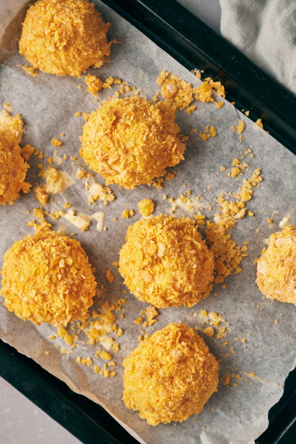 A baking sheet lined with parchment paper with cornflake coated ice cream balls.