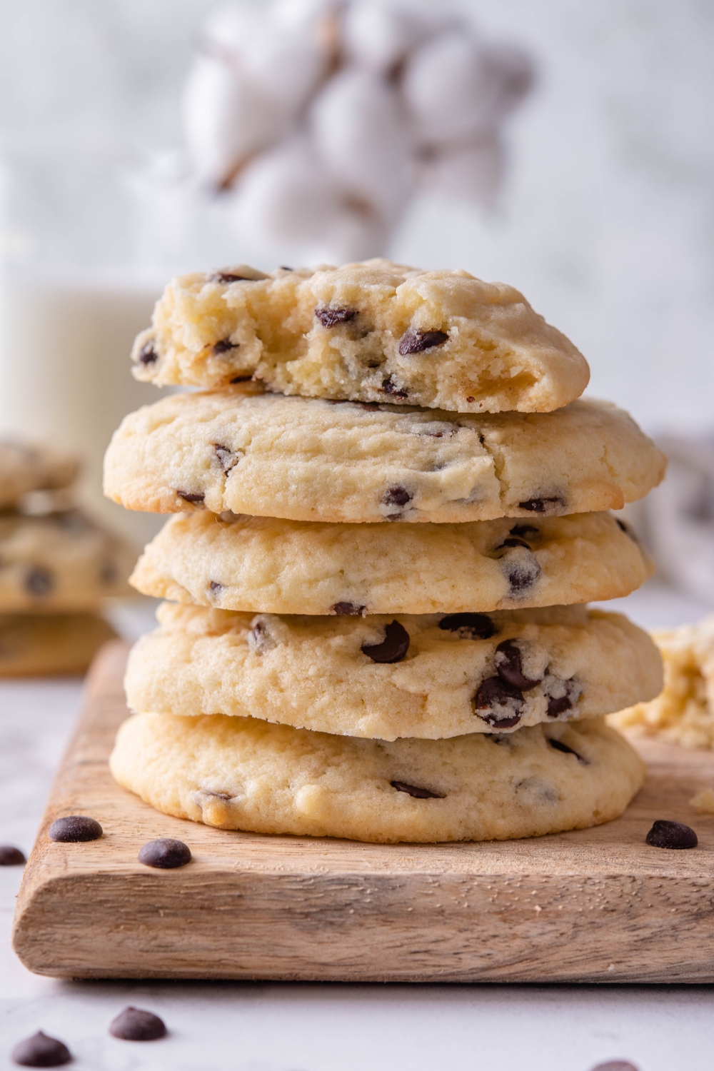 A stack of chocolate chip cookies with one cookie split in half on top sitting on a wooden serving board.