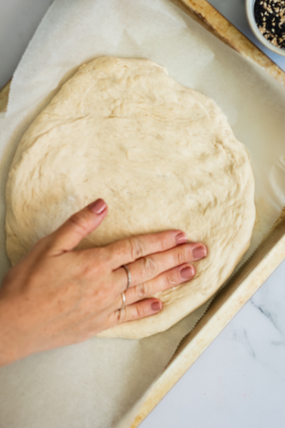 A hand flattening dough on a baking sheet.