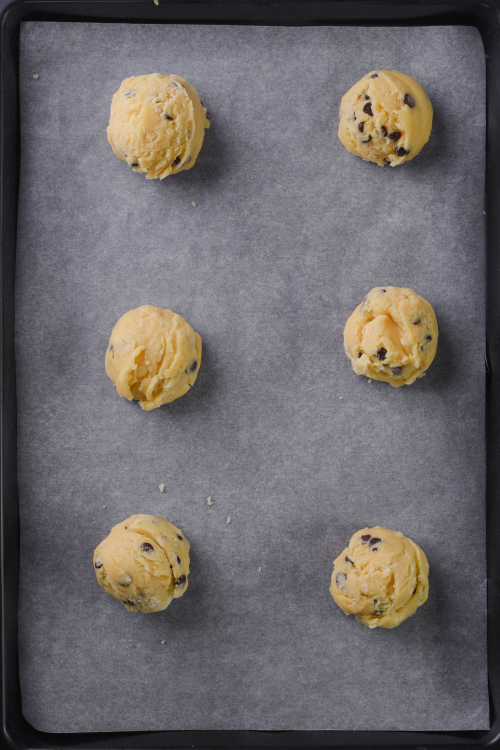 A baking sheet lined with parchment paper with 6 scoops of cookie dough on it.