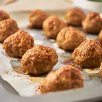A bunch of meatballs on a baking sheet lined with parchment paper on a baking sheet.