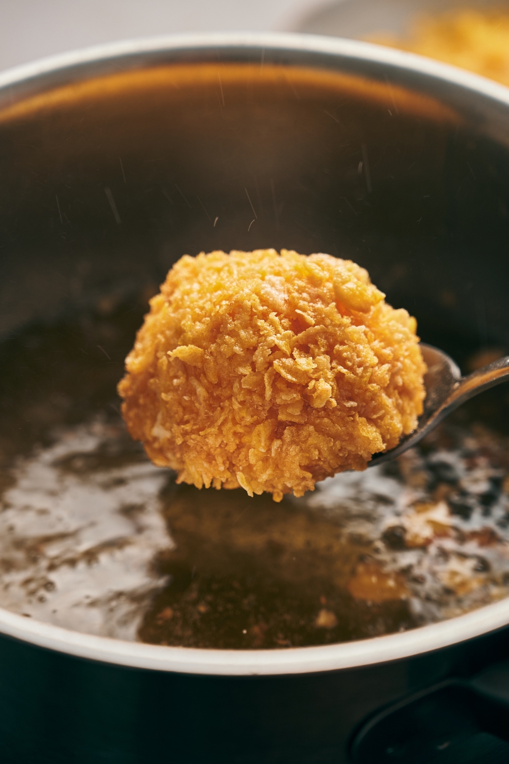A spoon is holding a fried ice cream ball over a pot with hot oil.