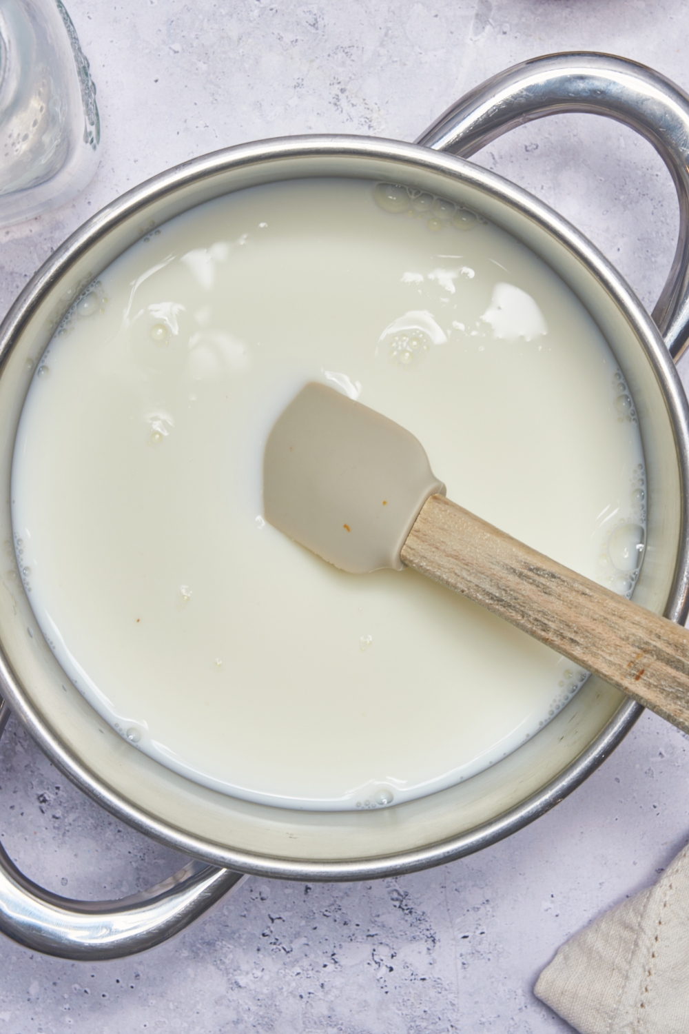 A sauce pot with milk in it; a rubber spatula is stirring.