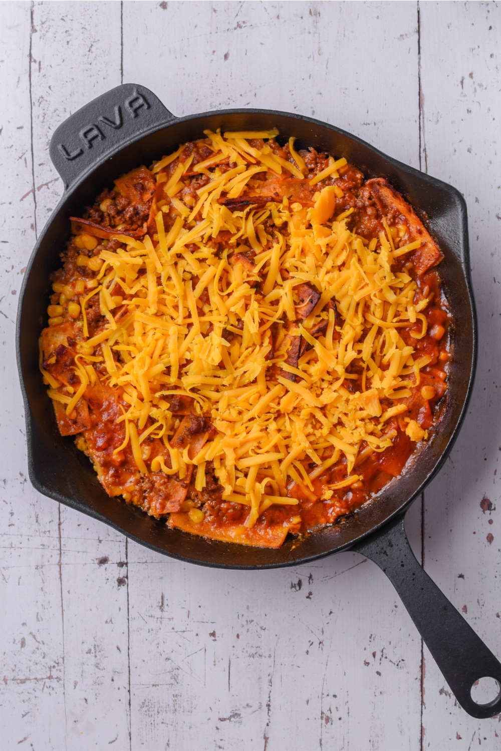 Shredded cheese on top of a frito taco casserole in a skillet.