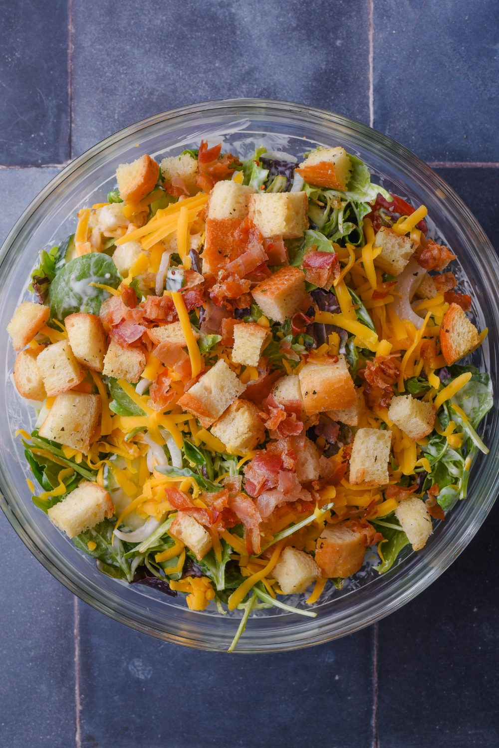 A mixing bowl with a house salad topped with croutons and bacon bits.