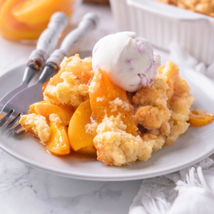 A scoop of vanilla ice cream on top of peach cobbler on a white plate.