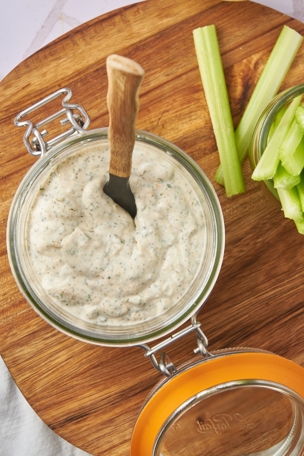 A mason jar with homemade ranch dressing in it. A jar with celery stalks is served next to it.
