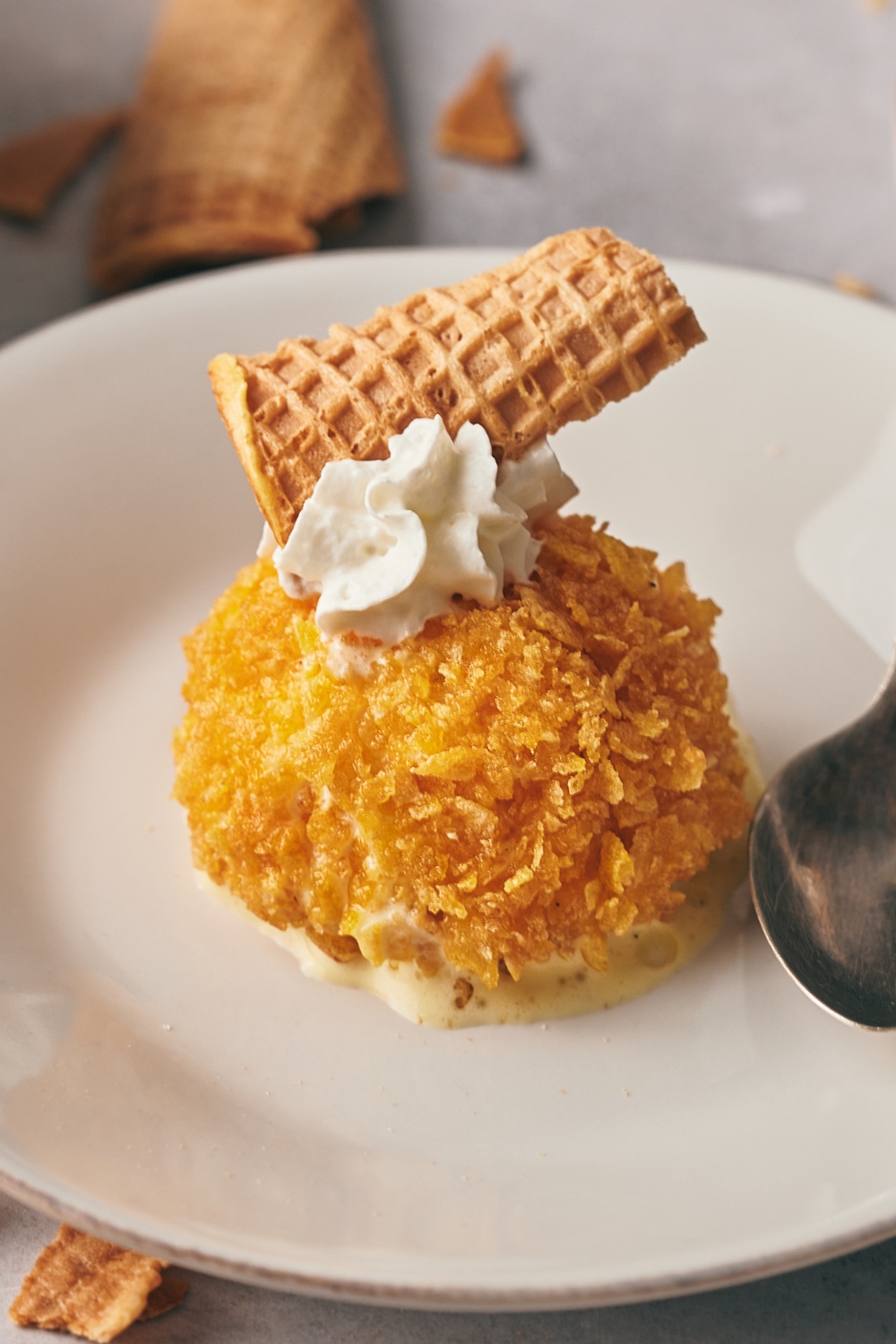 A plate with fried ice cream topped with whipped topping and an ice cream cone piece.