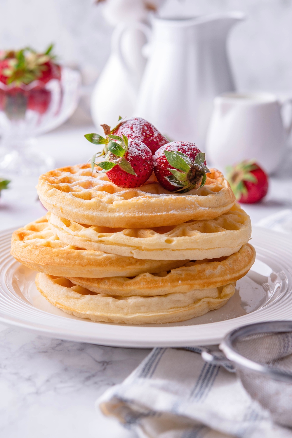 A stack of five mini waffles on a plate with strawberries on top.