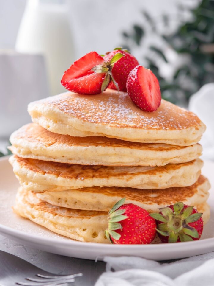 A stack of five pancakes with sliced strawberries on top.