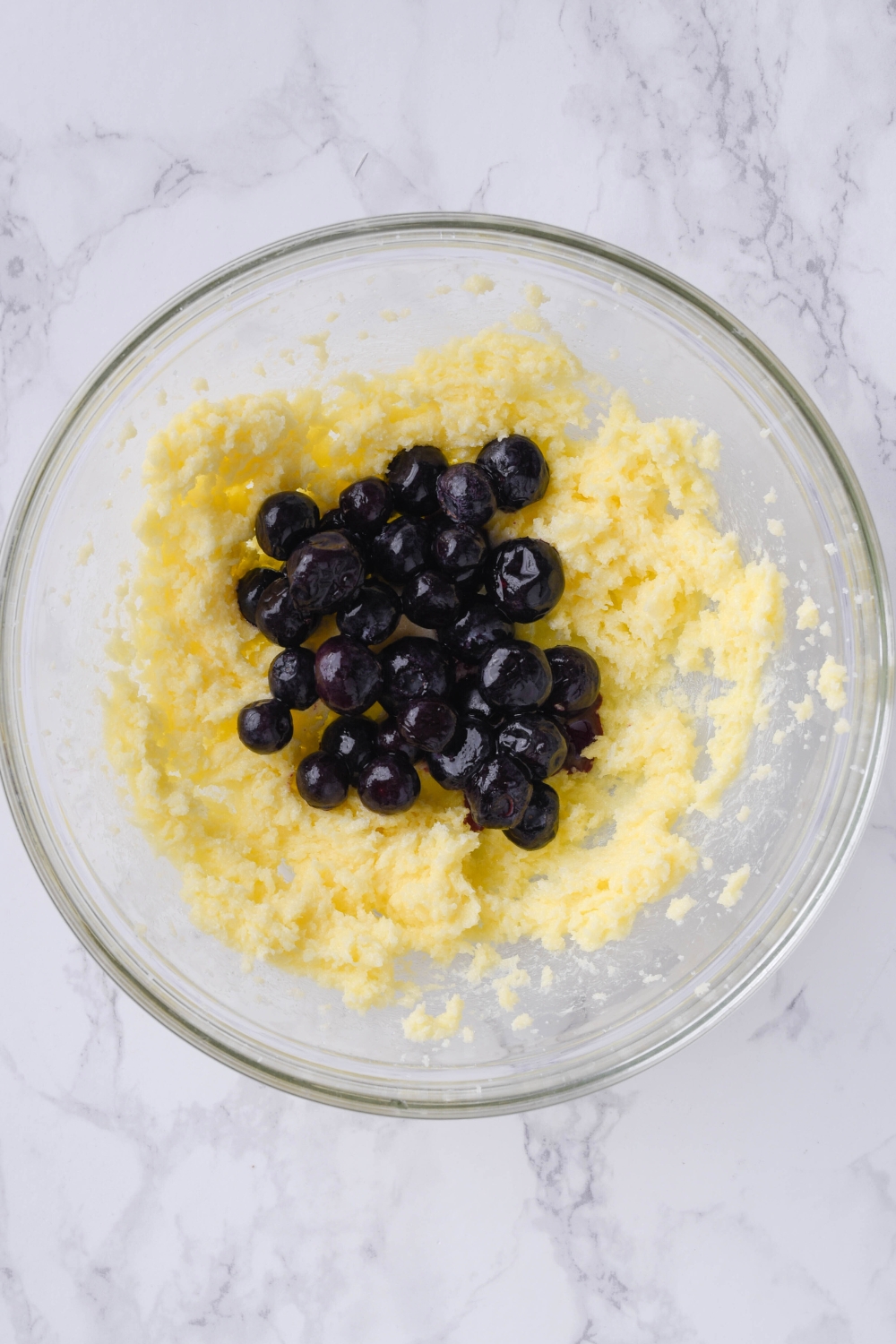 A mixing bowl with creamed butter. Blueberries have just been added to it.