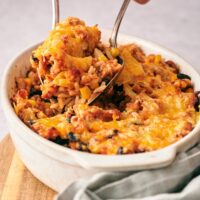 Two hands scooping taco casserole with rice out of a casserole dish filled with the casserole.