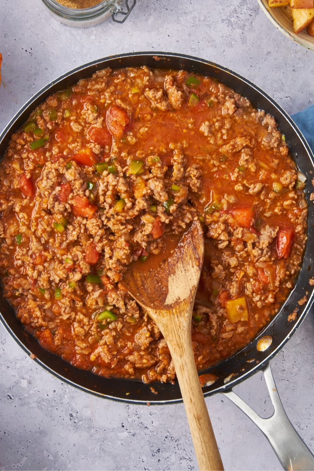 A large skillet with the ground beef mixture cooking with tomato sauce and diced tomatoes.