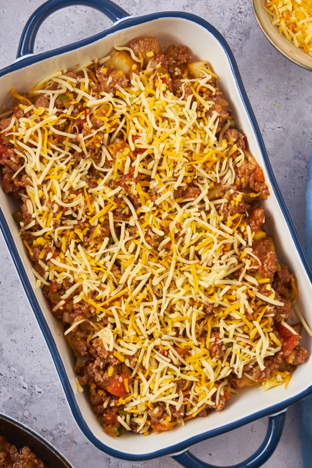 A casserole dish with a layer of potatoes and ground beef mixture topped with shredded cheese.