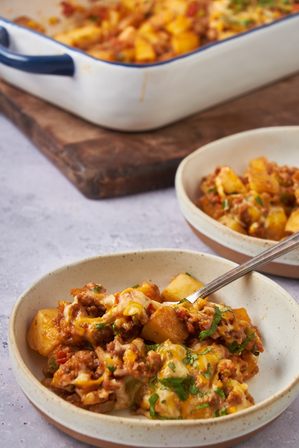 A bowl with taco potato casserole with a fork. The remaining taco potato casserole is in the background.