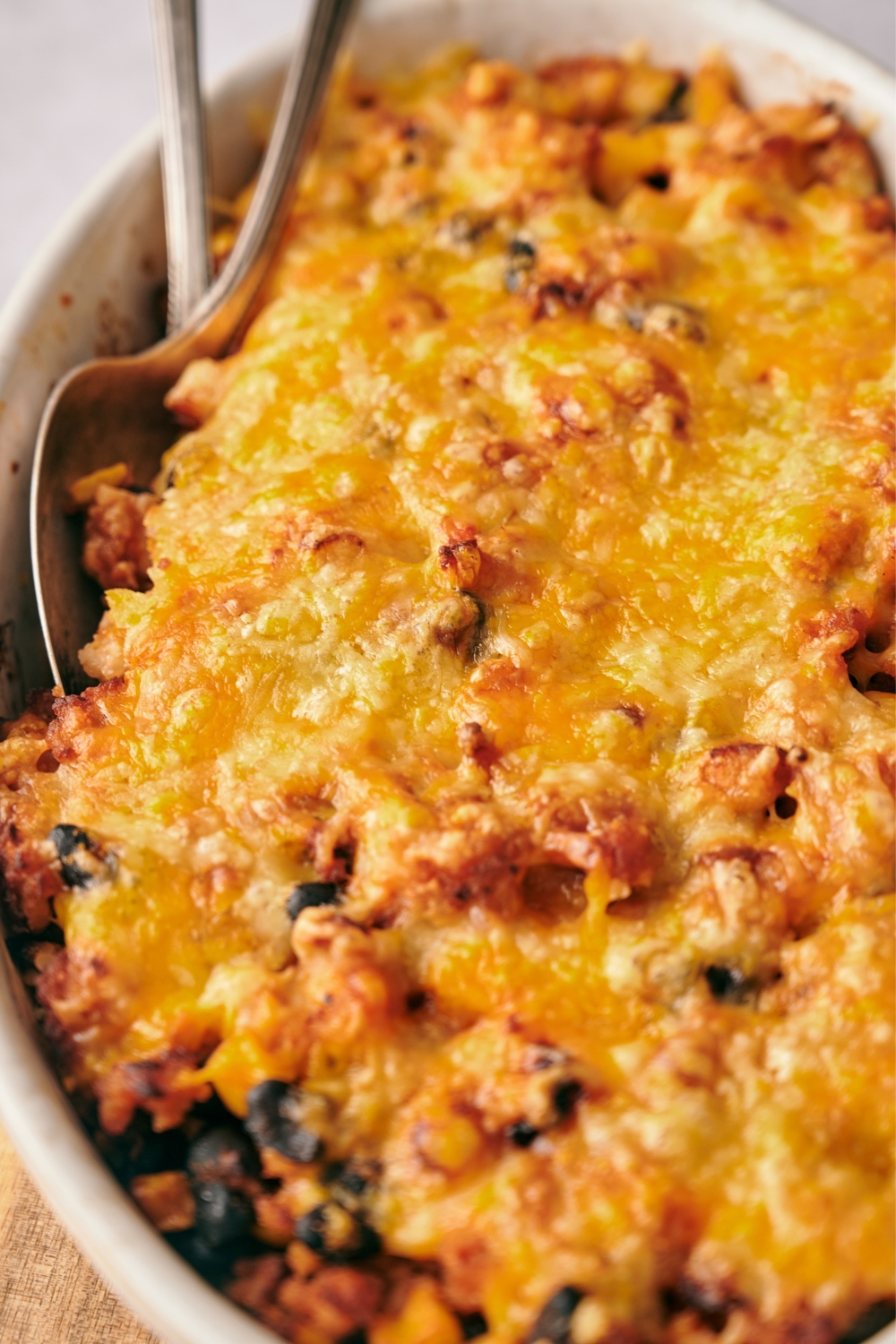A casserole dish with baked taco rice casserole. Two serving spoons are in the dish ready to serve.