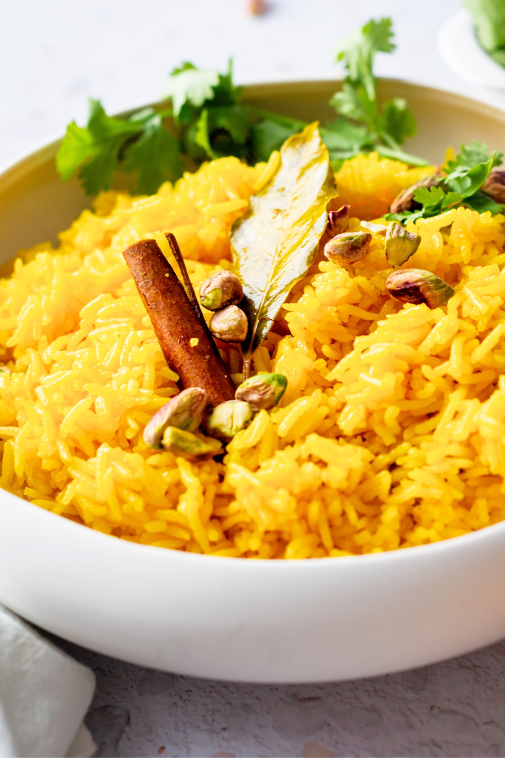A white bowl that has turmeric rice in it along with a cinnamon stick and bay leaf on top of the rice.