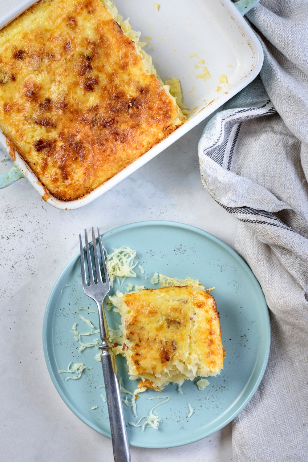 A square serving of Amish breakfast casserole on a blue plate with a fork on the plate and the rest of the casserole next to it.