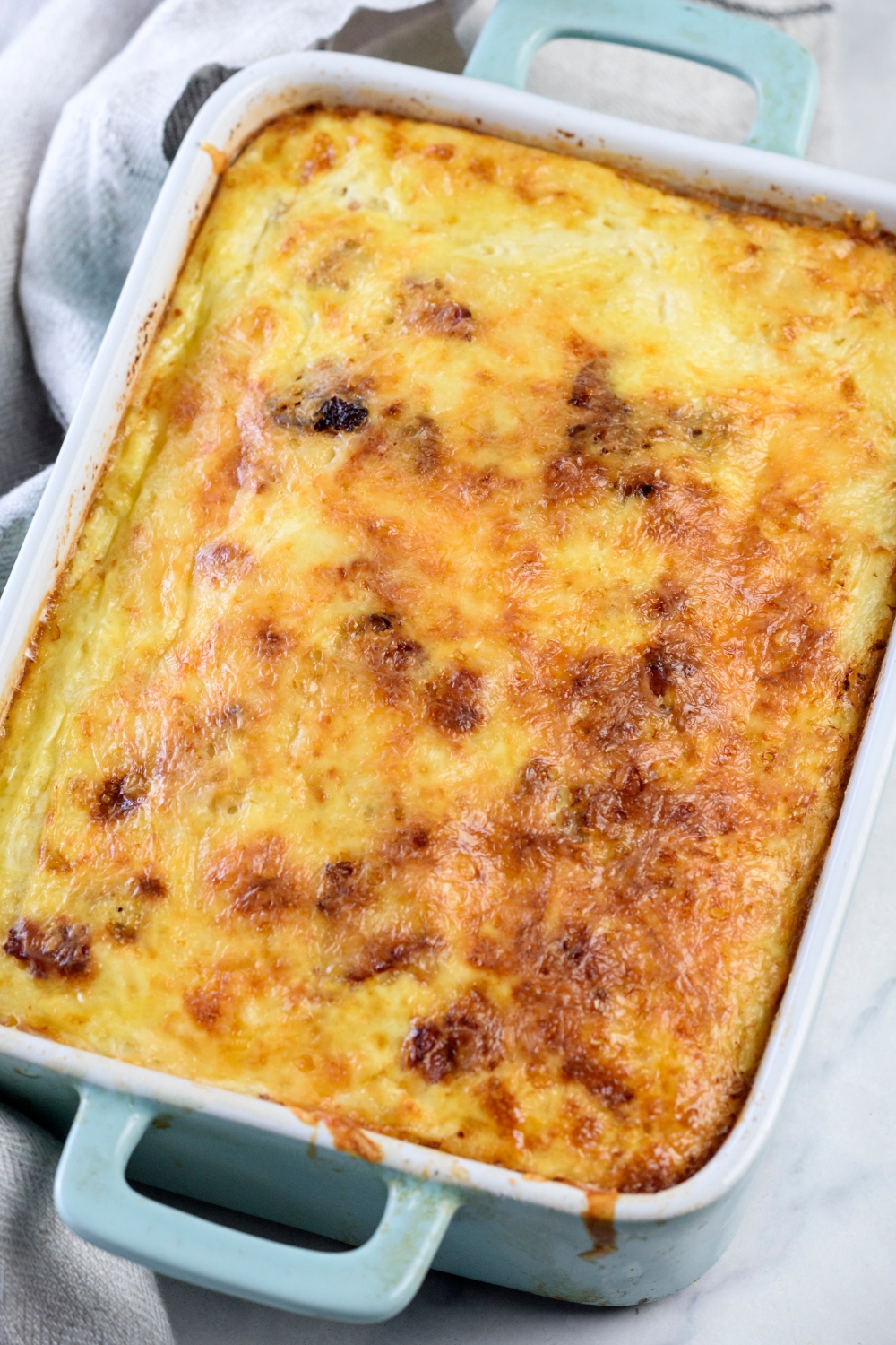 A baking dish filled with a freshly baked casserole covered in a golden brown layer of melted cheese.