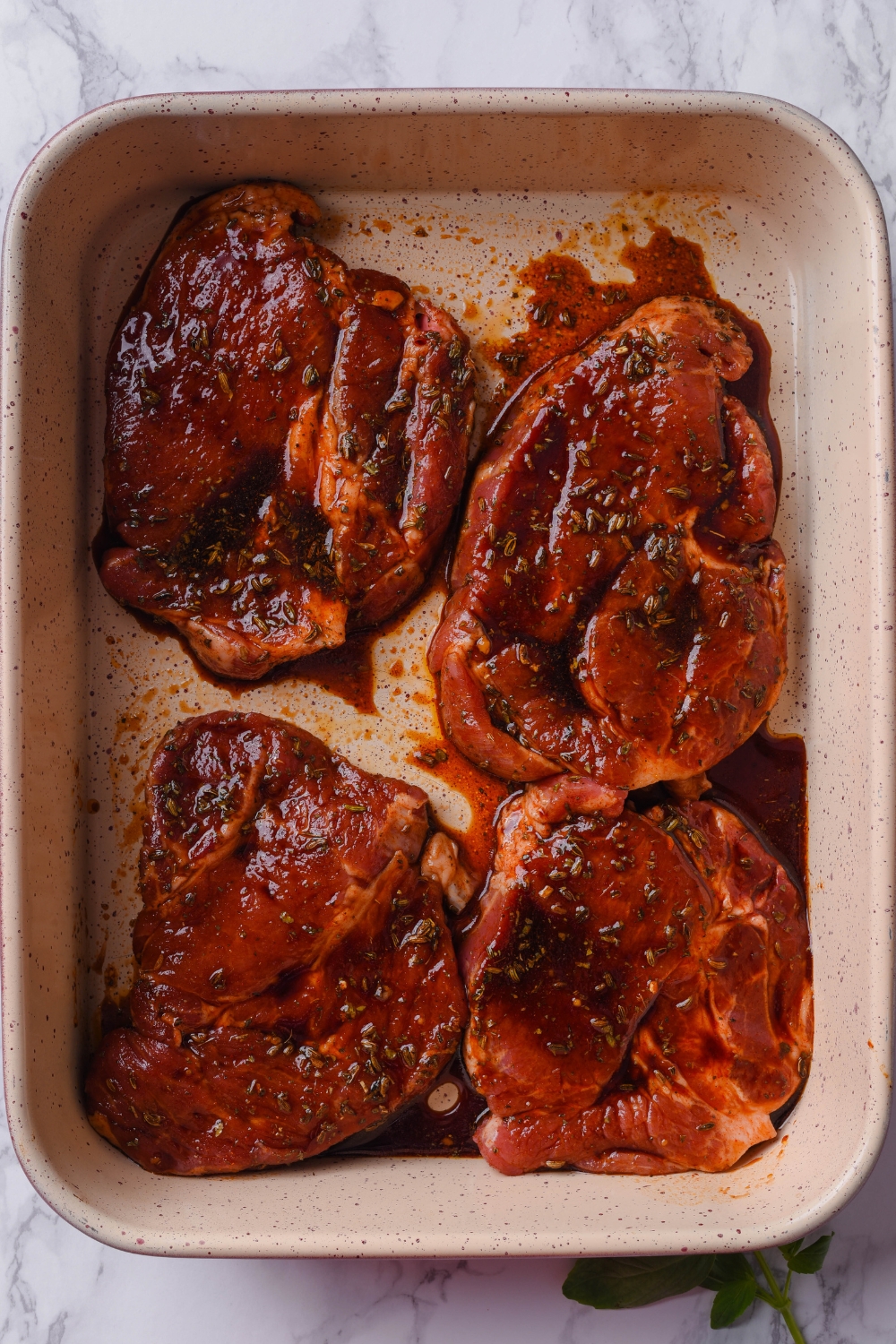 Four pork steaks in a baking dish covered in a brown marinade.