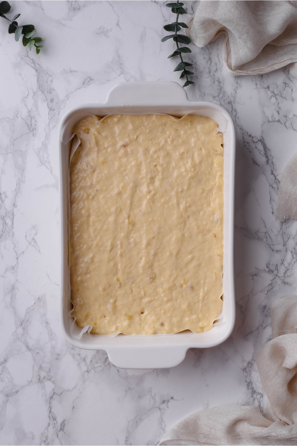 A white rectangular baking dish with a layer of parchment paper topped with cake batter.