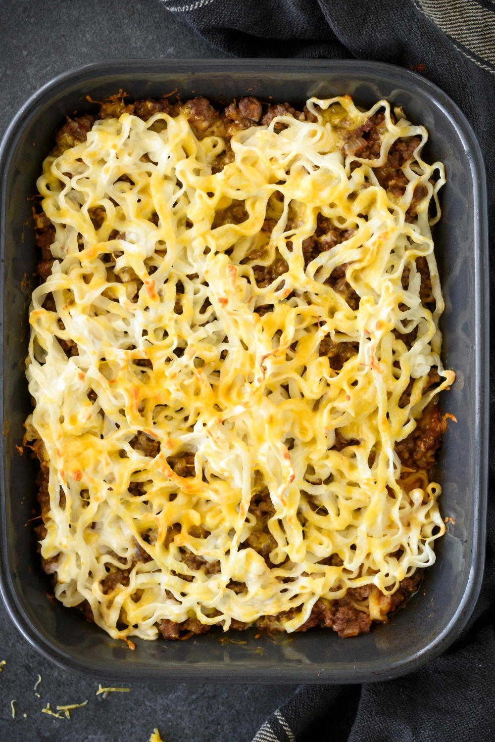 A baking dish filled with freshly baked hamburger and noodle casserole, covered with shredded cheese.