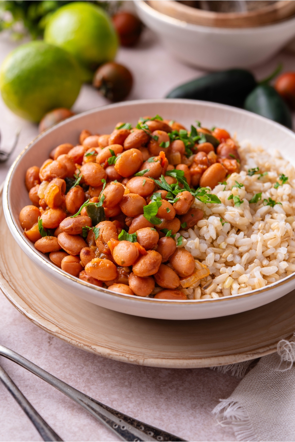 A bowl of Mexican pinto beans with a side of brown rice and fresh green herbs on top.