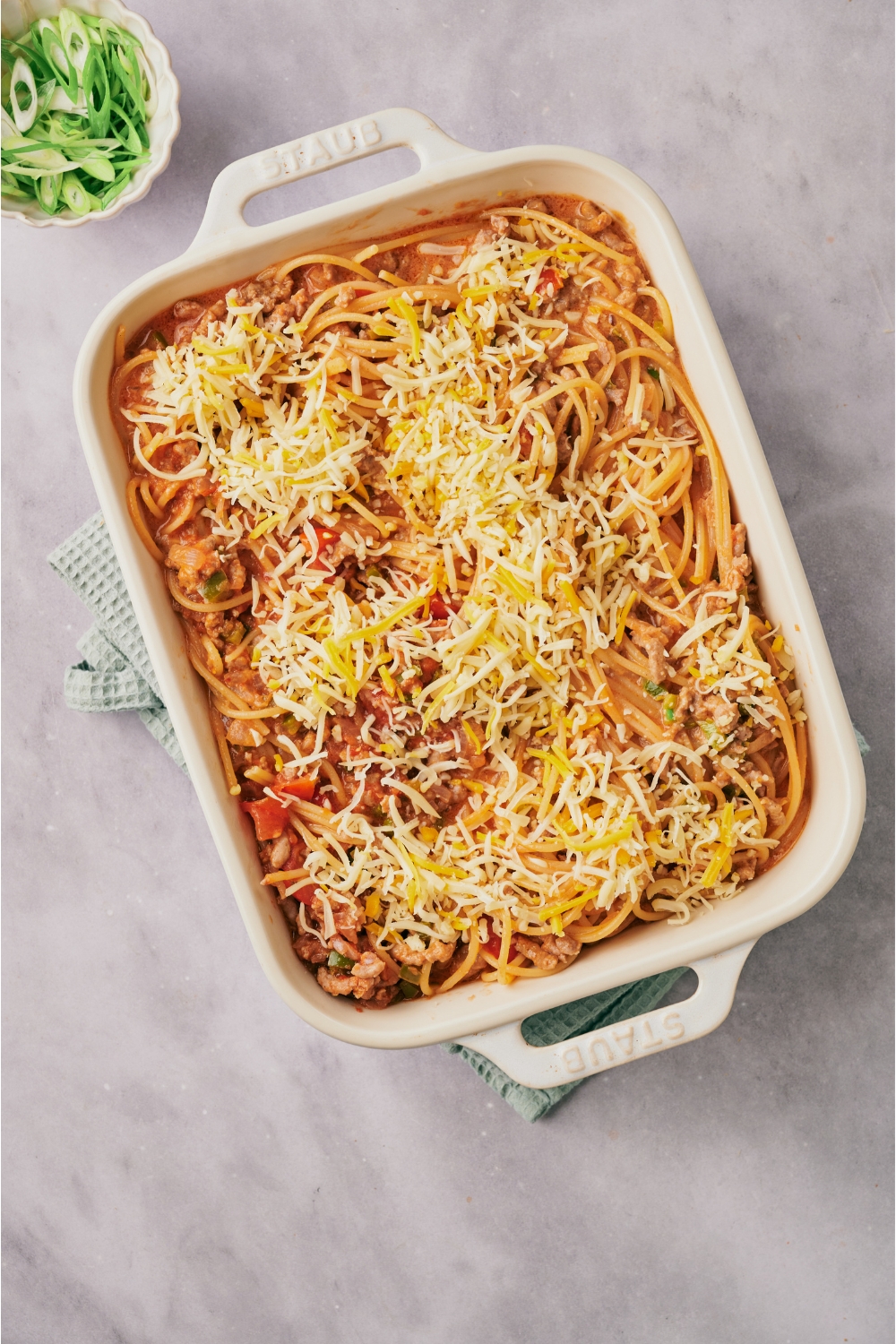 A white baking dish filled with spaghetti casserole covered in a layer of shredded cheese.