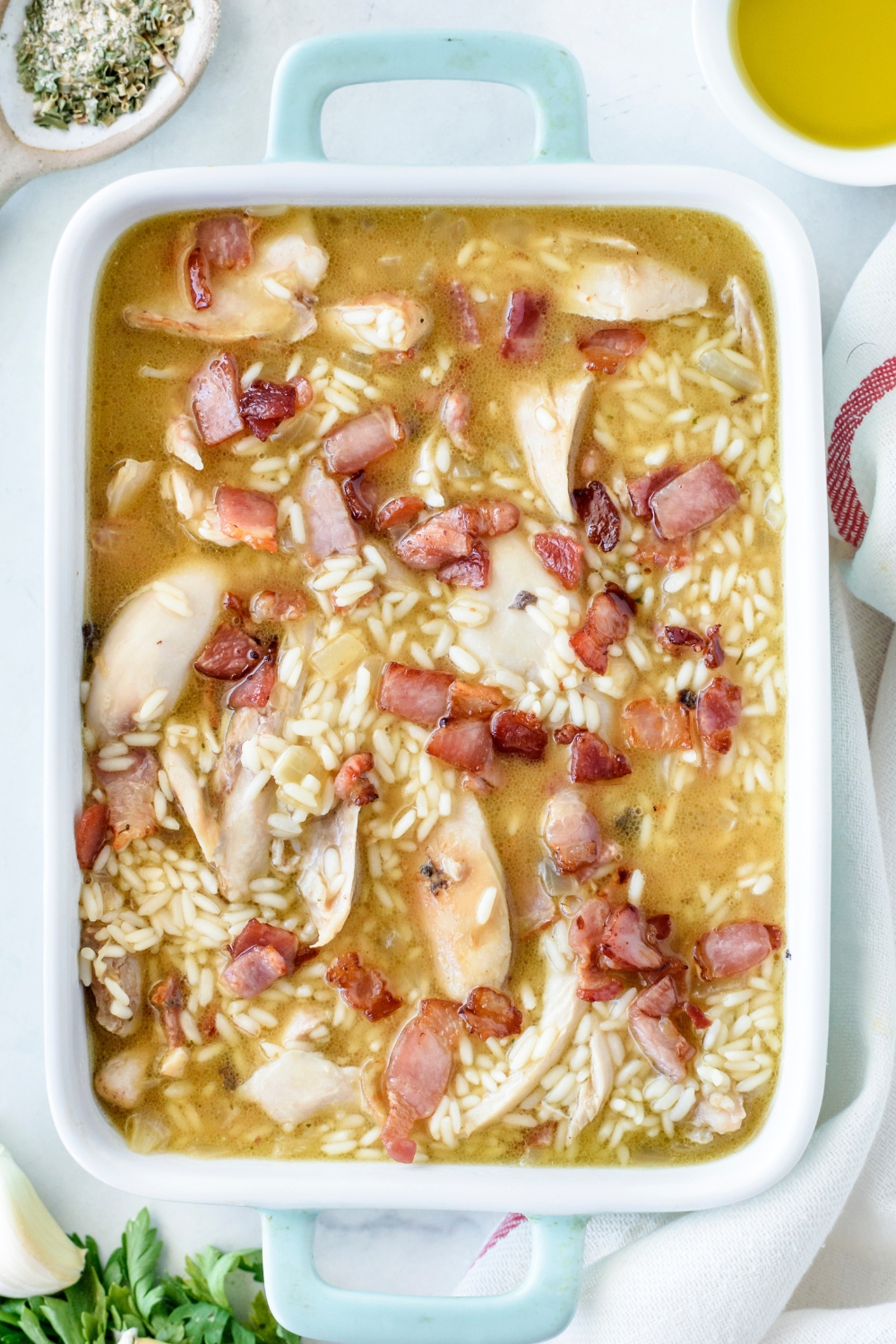 A baking dish filled with rice, cooked chicken, and cooked bacon, all covered with chicken broth to the top of the baking dish.