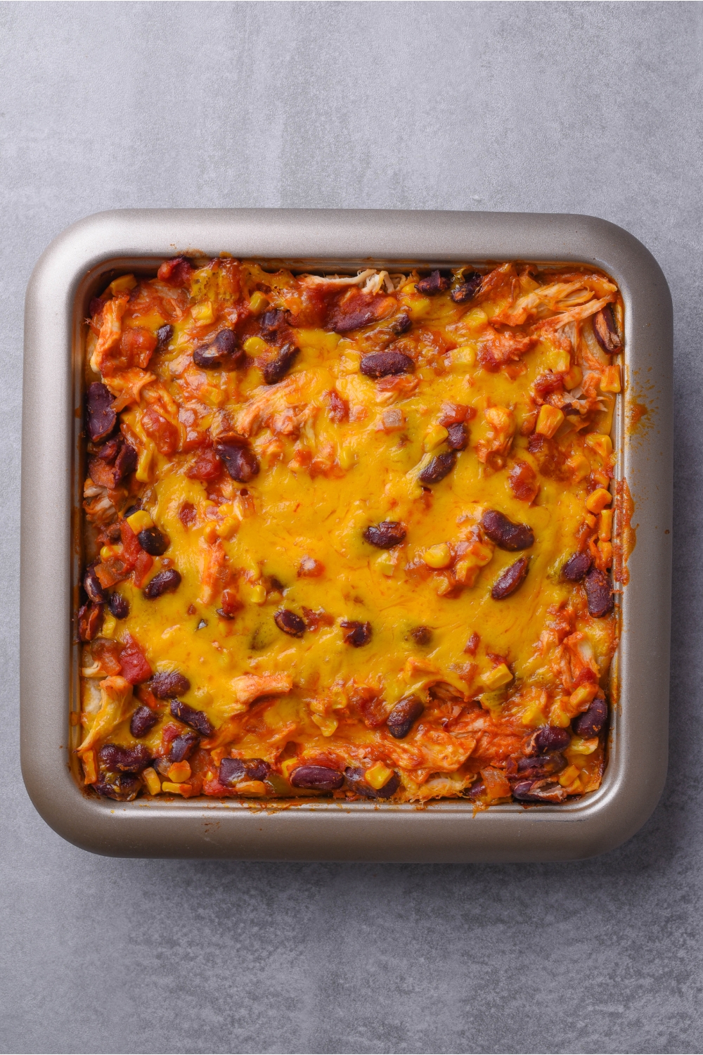 Square baking dish filled with a freshly baked casserole of shredded chicken, black beans, corn, tomato sauce, and melted cheese on top.