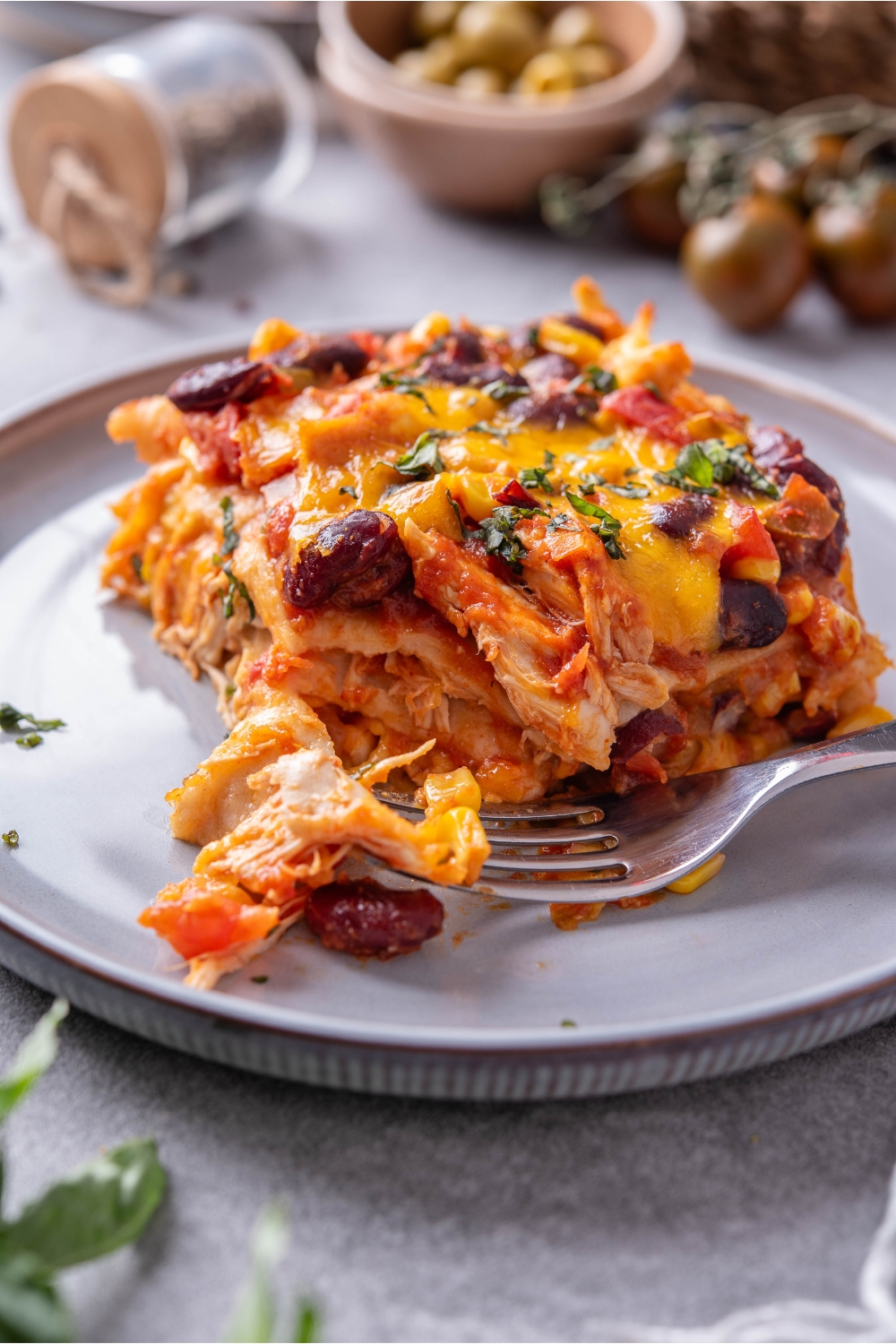 A serving of chicken tortilla casserole layered with shredded chicken, black beans, tomato sauce, melted cheese, and a bite has been taken out with a fork.