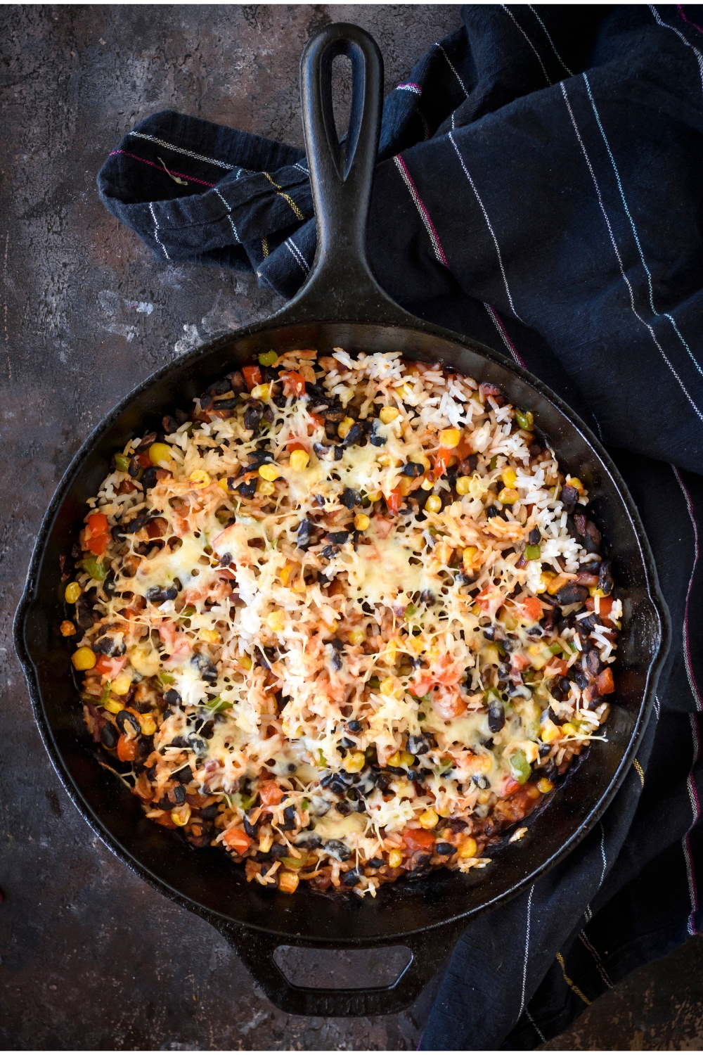 A skillet filled with freshly baked rice casserole covered in melted cheese. There are visible chunks of black beans, corn, and peppers.