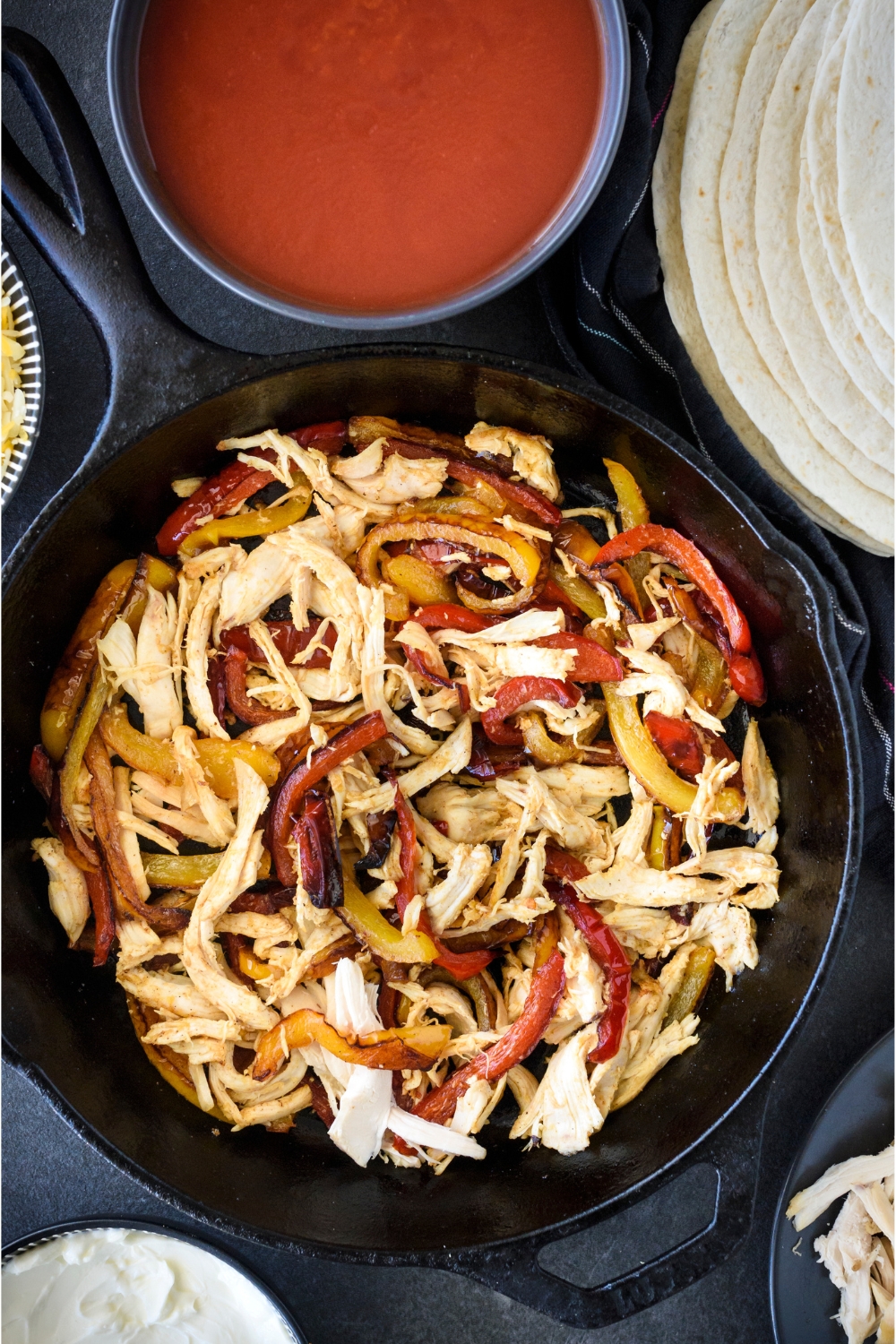 A black cast iron skillet with sautéed bell peppers and shredded chicken in it.